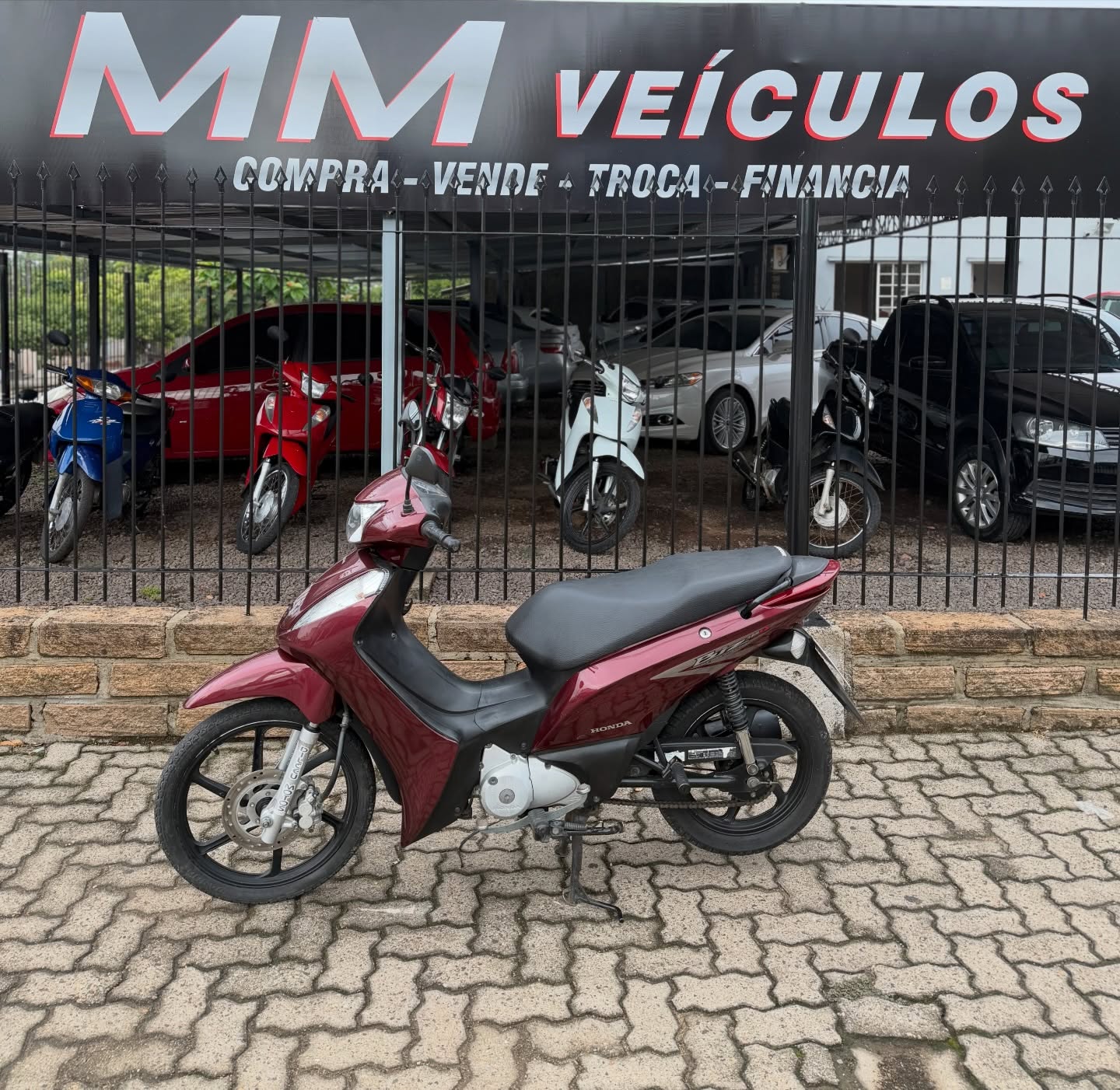 Honda Biz 125 EX 2012 vinho diante da fachada da MM Veículos