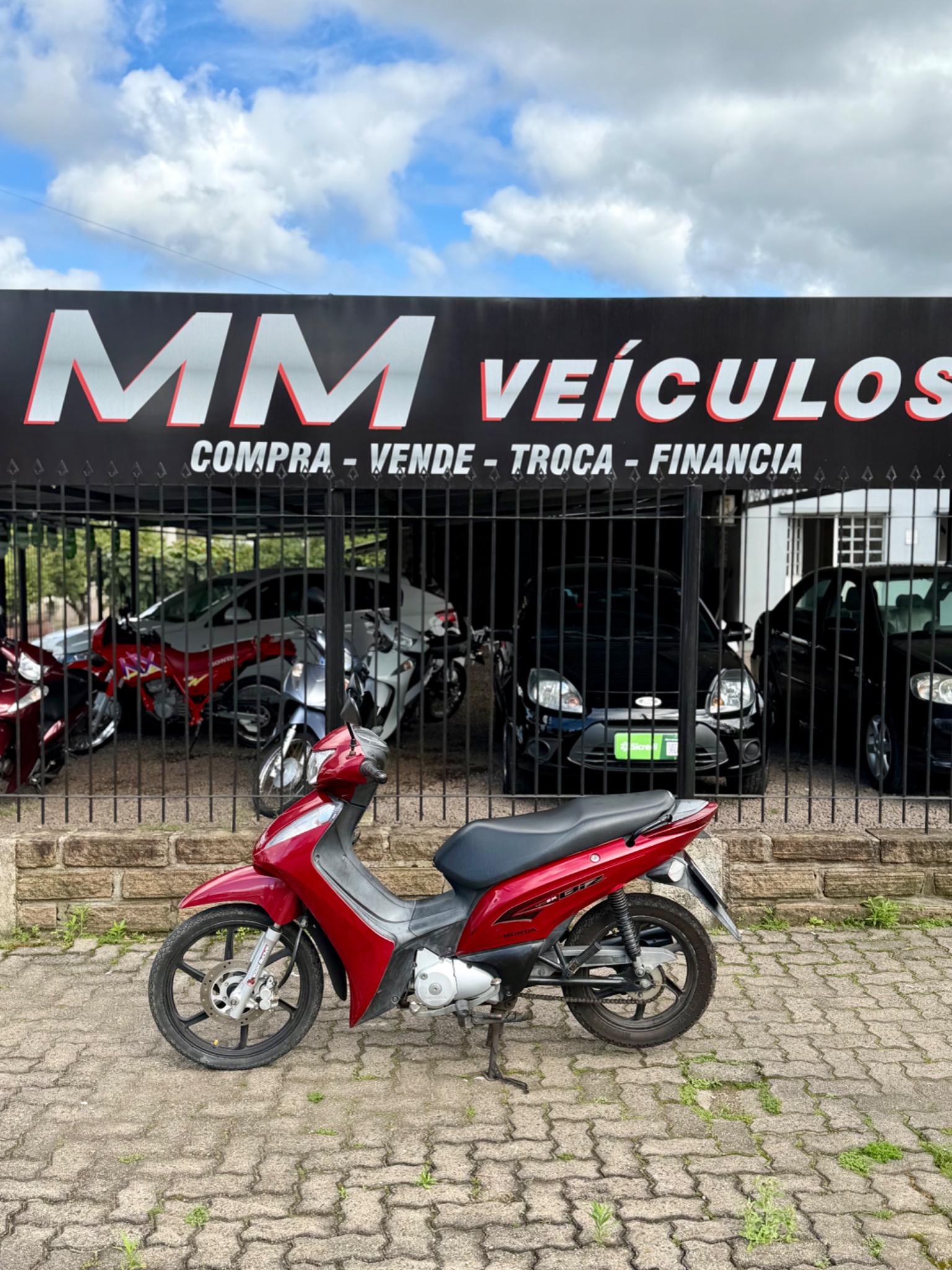 Honda Biz 125 EX 2013 vermelha diante da fachada da MM Veículos