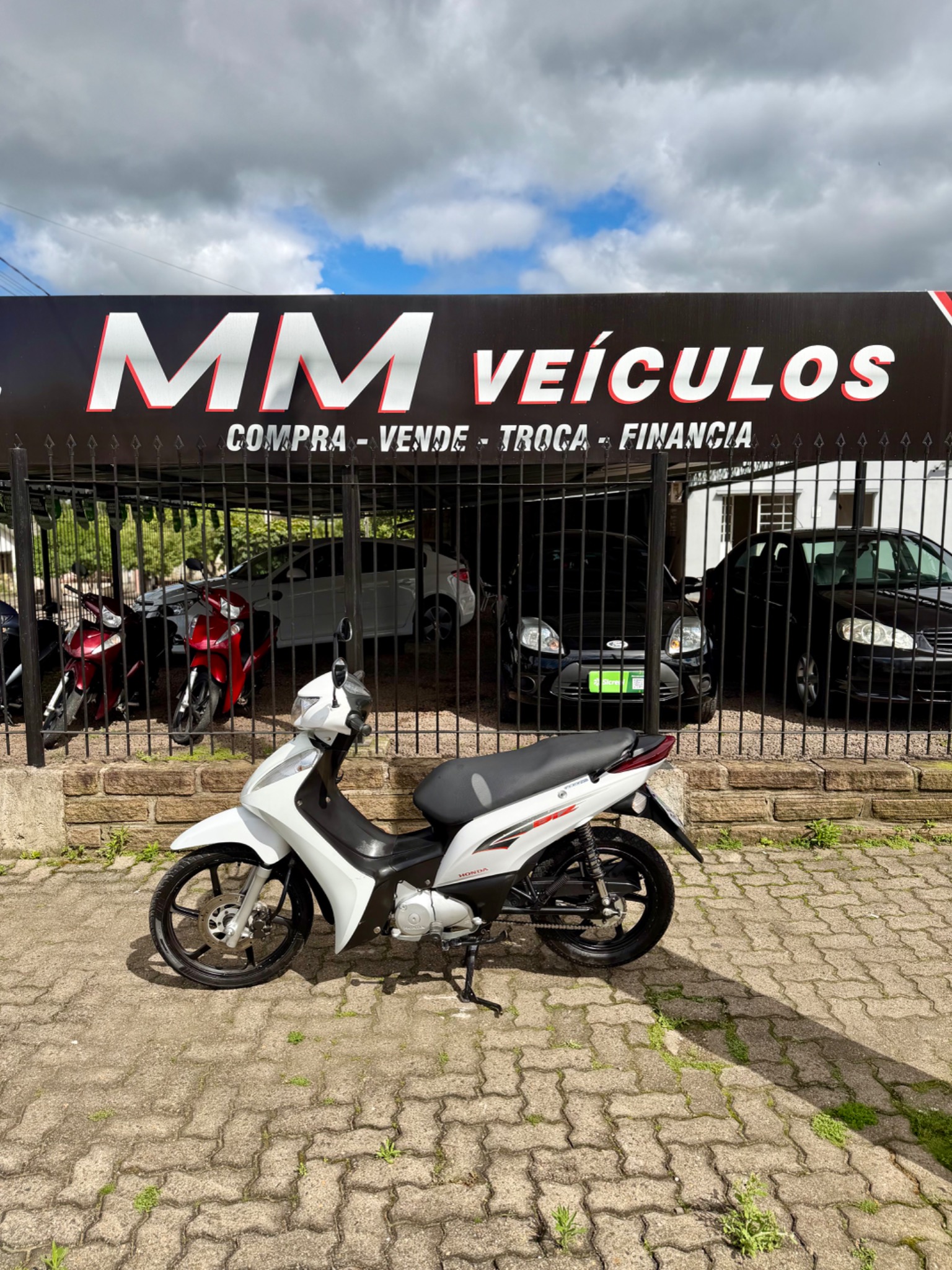 Honda Biz 125 EX 2014 branca diante da fachada da MM Veículos