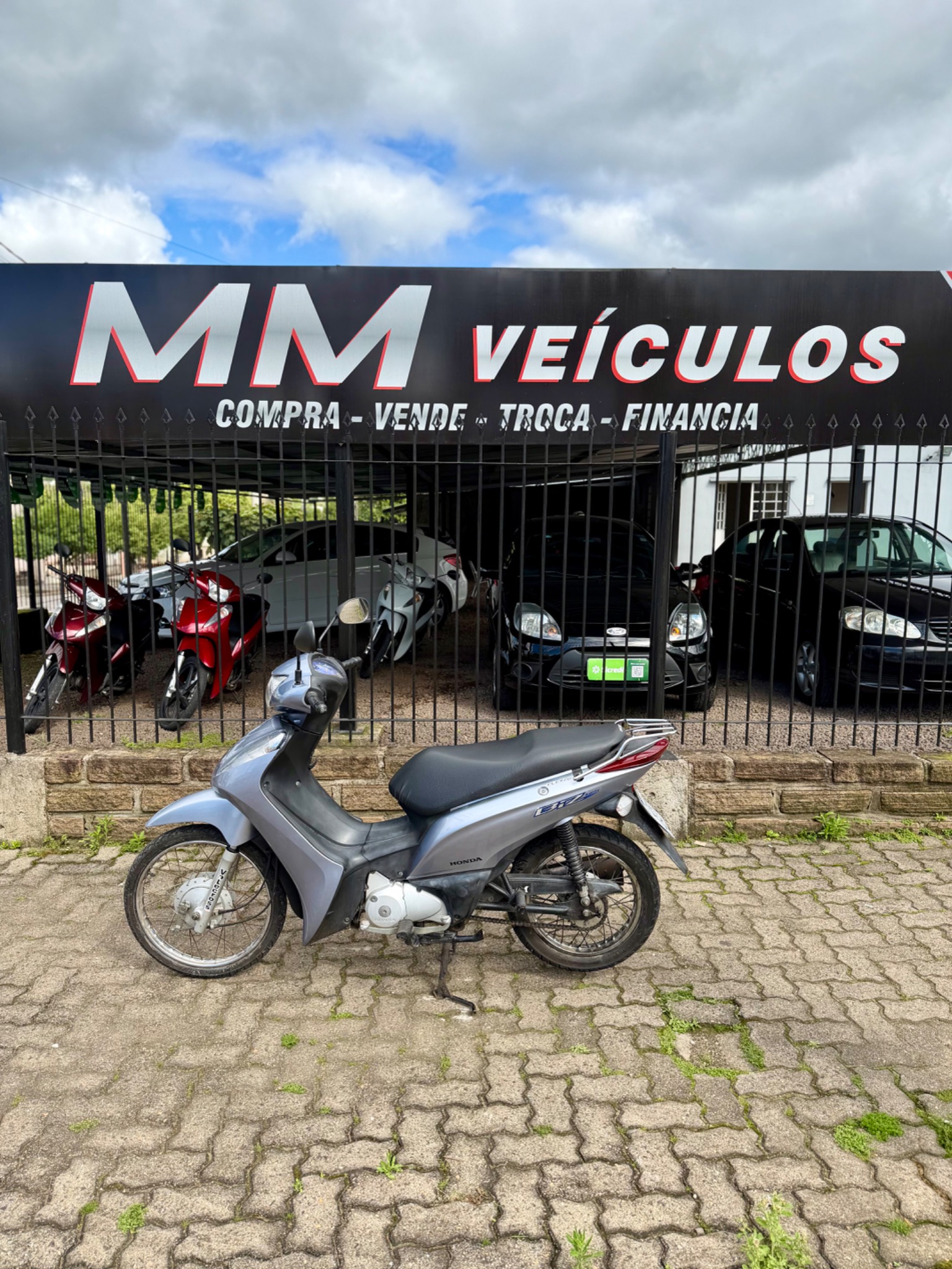 Honda Biz 125 ES 2015 cinza diante da fachada da MM Veículos
